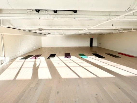 PtrBlt Miami Yoga Garage renovation photo of empty room with light wood floors and the silhouette of a person through sunlit windows.